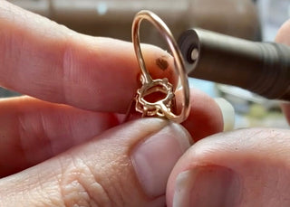 Rose gold ring held between fingers with a blurred background