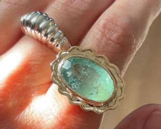 Silver ring with a green gemstone on a hand against a blurred background